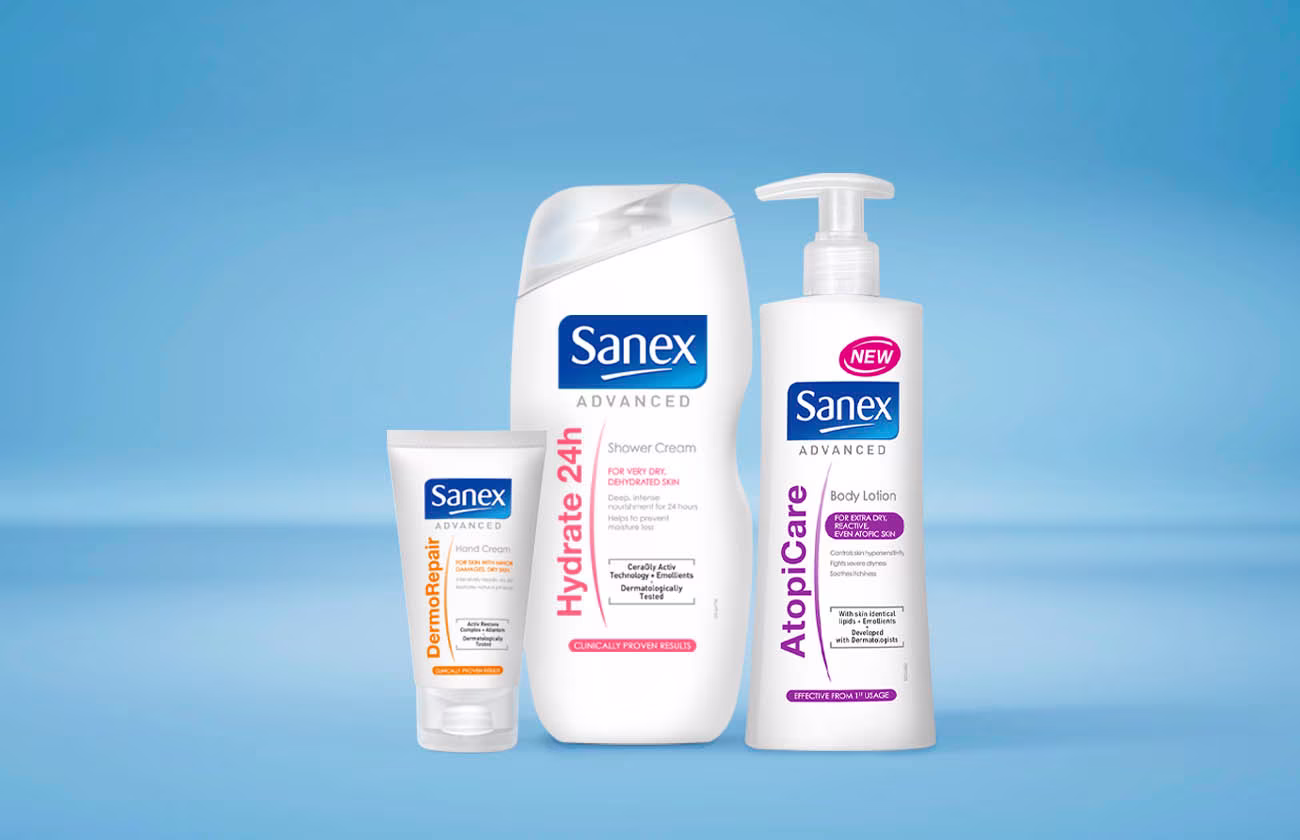 Drie producten uit de 'Sanex Advanced' lijn: een tube DermoRepair handcrème, een fles Hydrate 24h douchecrème en een pompflacon AtopiCare bodylotion.